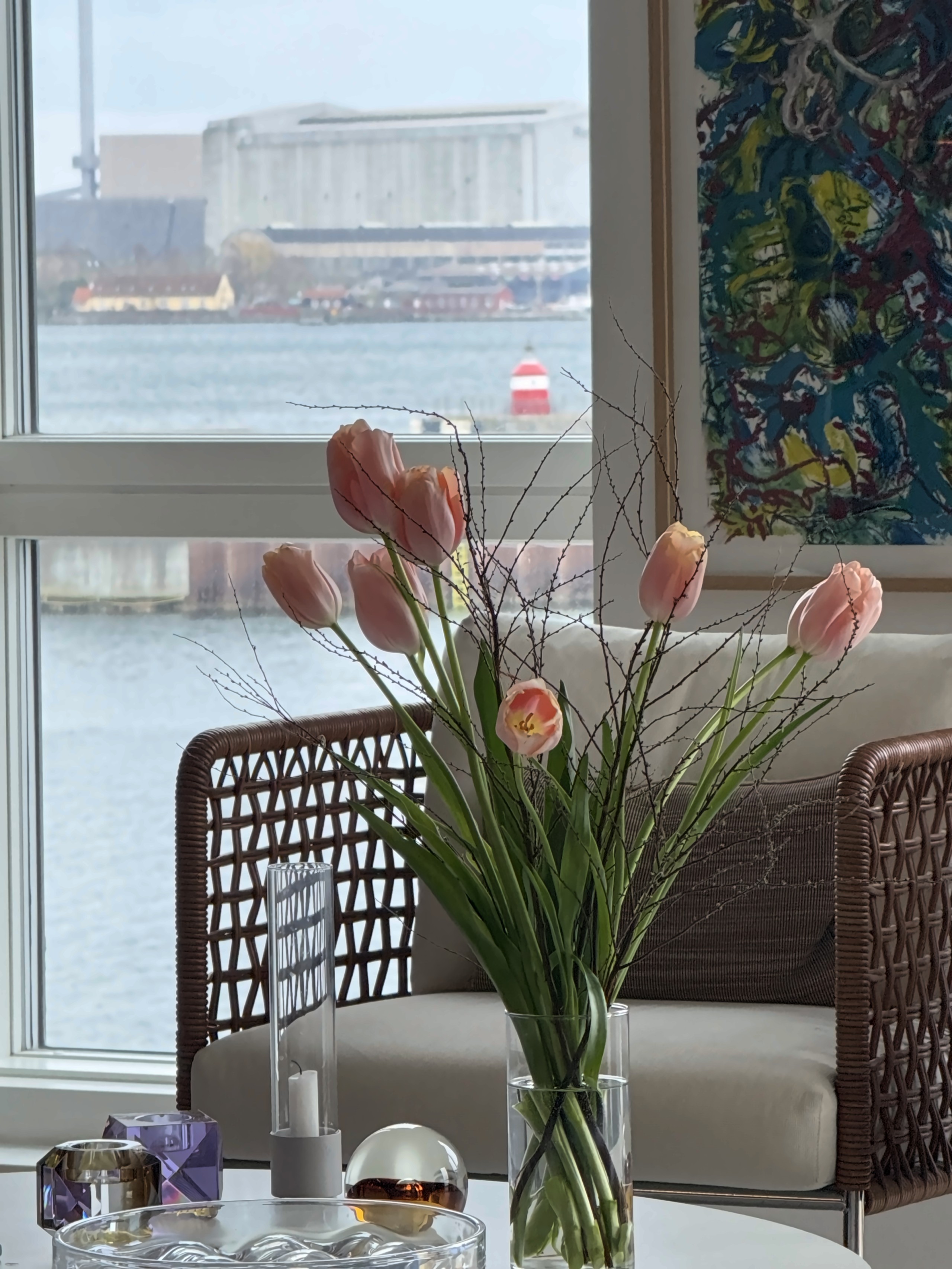 Lænestol og lyserøde tulipaner foran vinduet med havet i baggrunden