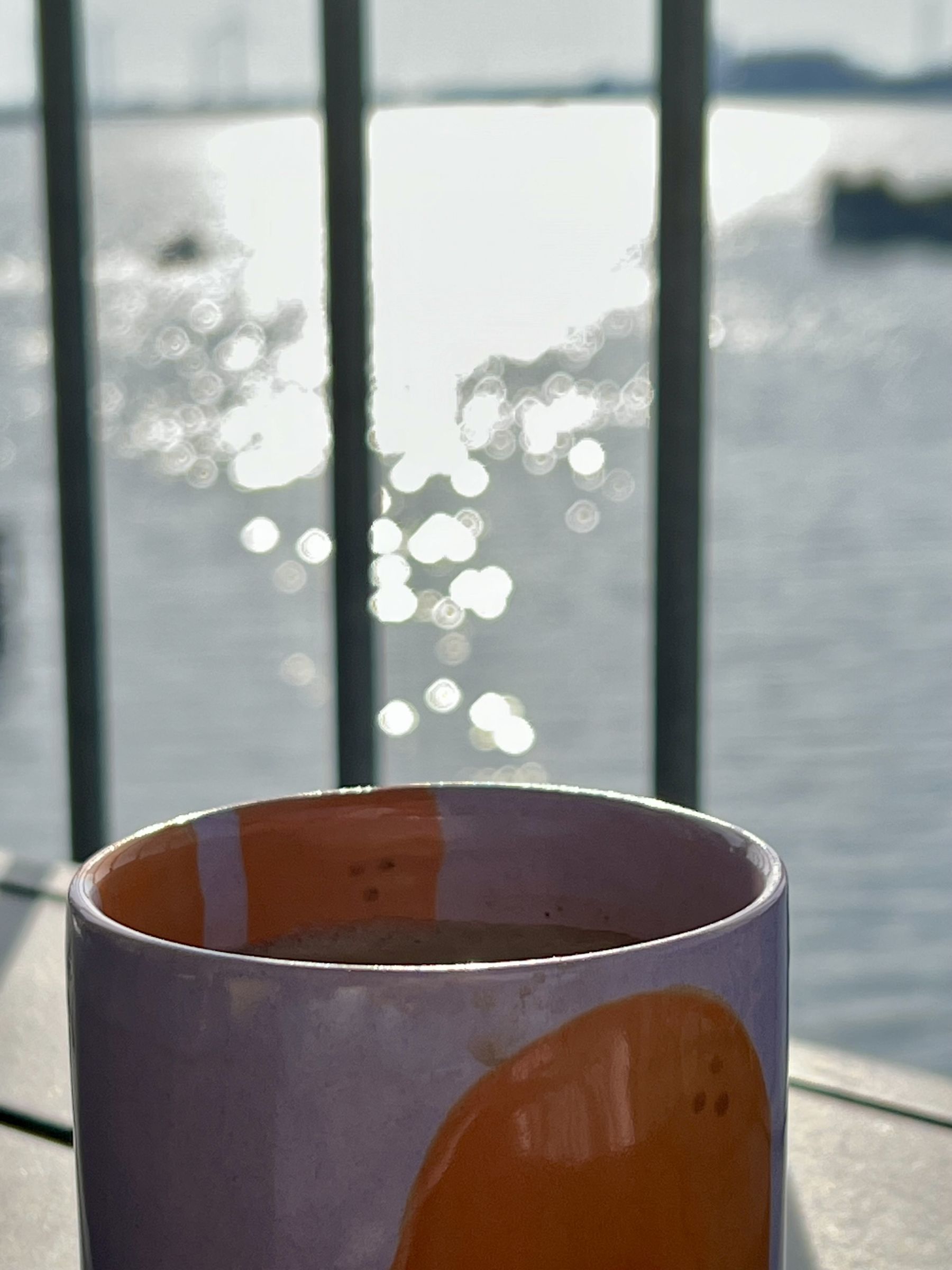 Kaffekop på altanen med glitrende vand i baggrunden